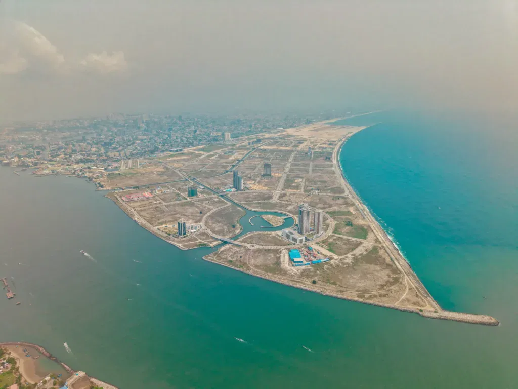 Aerial view of a coastal city with a narrow peninsula extending into the ocean, featuring a few high rise buildings, grid like roads, and a mix of developed and undeveloped land. The sea borders both sides of the peninsula.
