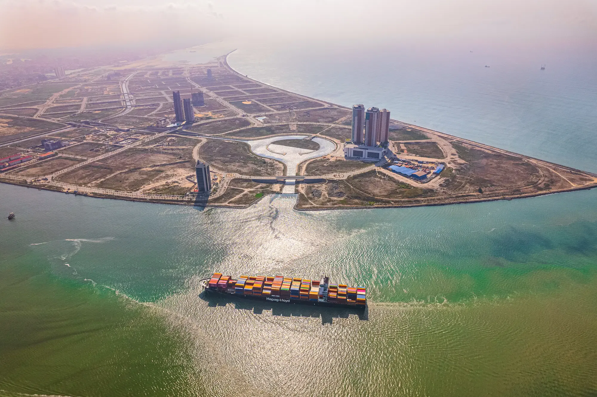 Aerial view of a container ship sailing near the coast of Lagos, with Eko Atlantic’s modern buildings and empty plots lining the sea.